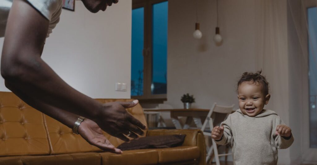 pexels-photo-6321641-6321641 A joyful father watches his baby take first steps in a cozy living room setting.